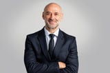 Portrait of caucasian business man looking at camera and smiling. Confident mature male professional is in suit. He is against gray background.